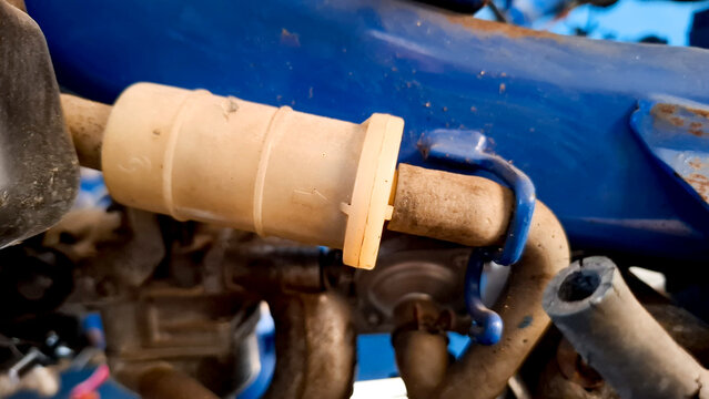 Close up view of a plastic inline motorcycle fuel filter connected to fuel lines mounted on a blue motorcycle chassis frame.