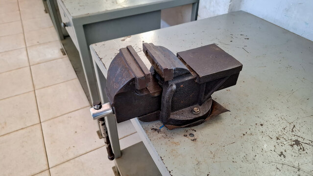 Heavy duty cast iron bench vise mounted on a metal workbench in a technical workshop or vocational classroom environment.