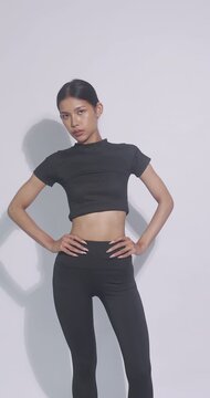 Asian fitness model posing with hands on waist. Confident woman in black sportswear smiling at camera.