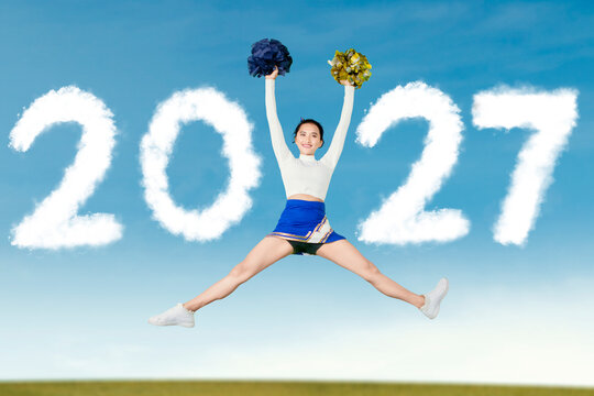 Joyful Asian Cheerleader Jumping in the Air with 2027 Cloud Text Sky Background