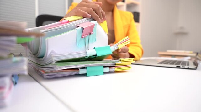 Organized Chaos: A person sorts through a large stack of documents, meticulously organized with colorful clips and sticky notes, highlighting the detailed work of office administration.
