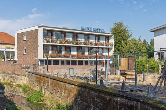 Valkenburg, Netherlands - October 04, 2026: Marx Motel exterior with vibrant flower balconies next to stone canal wall of Geul river on clear autumn day.