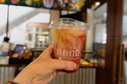 Bangkok, Thailand - October 14, 2026: Close up of a hand holding a Luk Kko brand blended fruit smoothie in a plastic cup with a blurred cafe background.