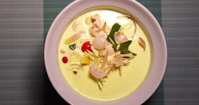 Traditional Thai Tom Kha Gai coconut chicken soup in a white bowl. Creamy spicy soup with galangal, lemongrass, kaffir lime leaves, and chicken. Authentic Asian cuisine served for dinner.
