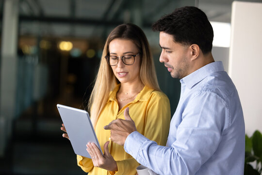 Two young male and female coworkers discussing online presentation or ideas using digital tablet, looking at device screen, analyzing business metrics, reviewing project data or new corporate platform