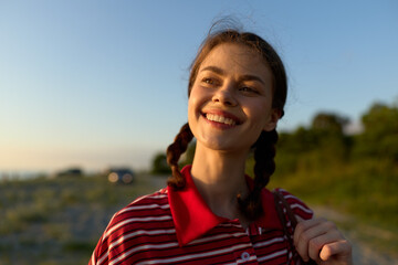 Fototapeta premium A smiling young woman enjoying lifestyle outdoors on a summer day. The happy female with braided hair looks at the sunlight, urban travel concept, authentic natural beauty portraits.