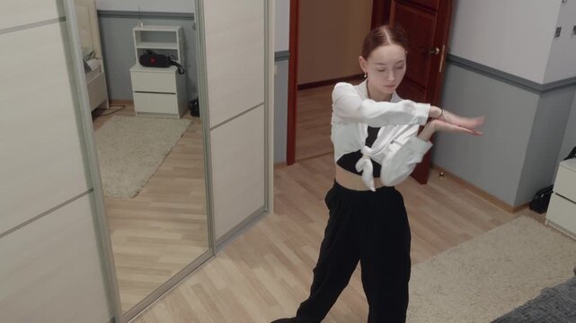 Woman wearing white shirt, black pants dancing solo down office hallway, executing twisting torso movement while looking downward, showing focused expression, wooden flooring.