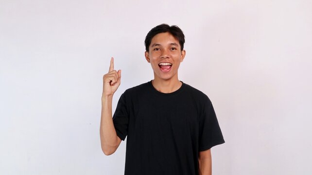 Cheerful young Asian man smiling with an open mouth while raising his index finger up in an eureka idea gesture against a white background.