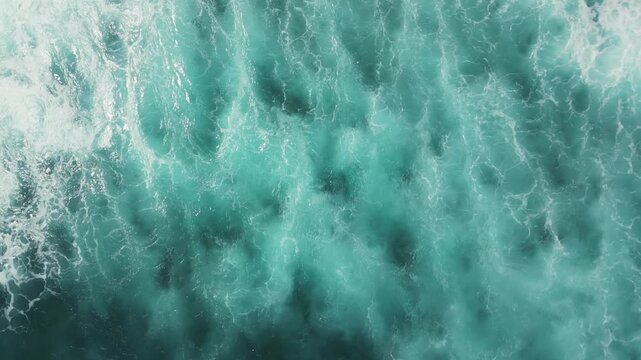 Turquoise ocean waves crash and spread into white foam, leaving swirling patterns on the water.