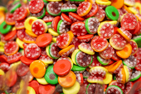 Colorful assorted gummy candies with intricate red and white patterns in a closeup view, bright green yellow orange and red chewy sweets creating a vibrant candy background.