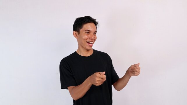 Happy young Asian man laughing cheerfully in side profile while miming driving a steering wheel with his hands against a white studio background.