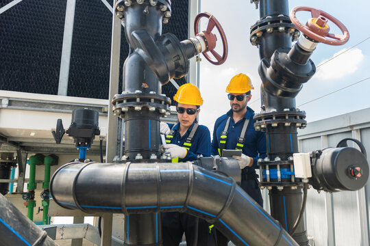 Engineers inspecting cooling tower water pipe system at industrial plant, Technicians checking pipe valves on building rooftop, Worker using wrench and digital tablet to service cooling tower pipeline