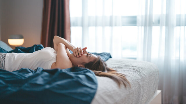 Asian woman yawning on bed relax lying in messy bedroom in morning