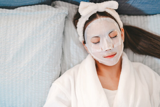 Relax young adult asian female wearing bathrobe with beauty face mask closed eyes, sleeping on bed