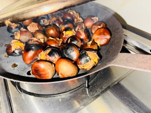 Roasted chestnuts in a black perforated roasting pan with open shells, autumn food close-up