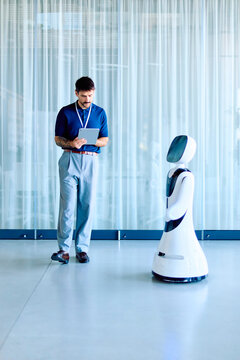 Man interacting with a humanoid service robot, programming its functions with a digital tablet in a modern office environment