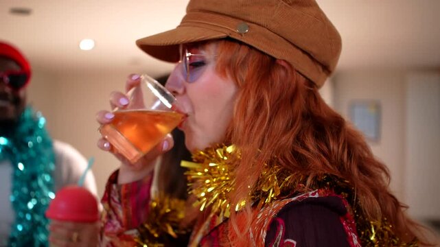 Multiethnic friends having fun and dancing together at a house party. An african american man in sunglasses and a tinsel boa smiles and sings for the camera while his friends drink in the background