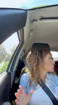 Annoyed curly-haired woman gesturing and having a heated conversation while driving her vehicle on a sunny day, expressing frustration and anger during her commute or road trip