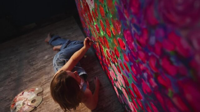 Child paints vivid flowers on a large canvas. Colors explode in bold, joyful strokes. Focus is intense, movement is fluid. Artistic expression radiates creativity. Perfect for creative, educational