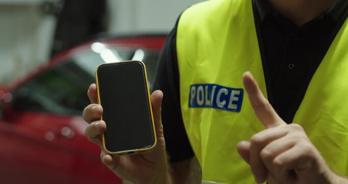 Police officer holding a smartphone and giving a warning gesture. Concept for prohibited phone use while driving, road safety, traffic rules and distracted driving.