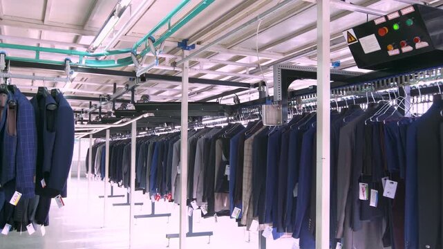 Automated garment sorting conveyor system array of men suits women dresses, hanging on automated clothes distribution center warehouse in retail shop, robotics logistics technology production line.