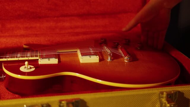 Hands lift a sunburst electric guitar from a tweed case.