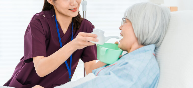 介護用コップで水を吸い飲みさせる介護士,看護師の女性と入院患者の高齢者女性