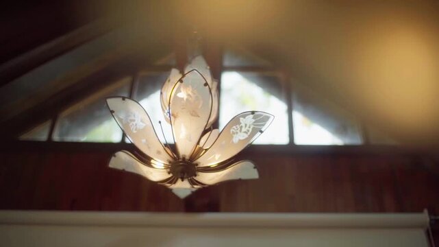 Slow motion flower shaped glass ceiling lamp glowing under wooden roof