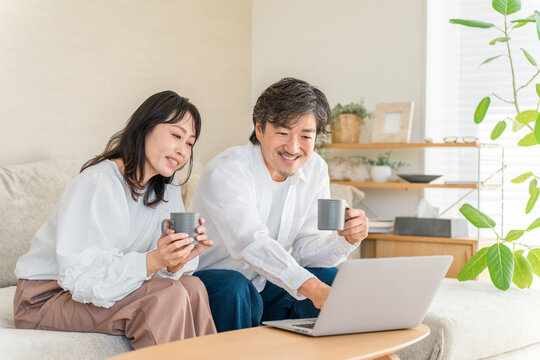 Close Middle-Aged Couple in Their Forties or Fifties Enjoying the Internet While Drinking Coffee and Looking at a Laptop in the Living Room