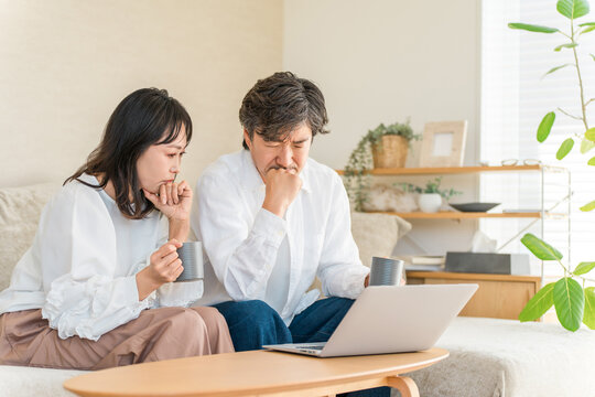 リビングでノートパソコンを見ながら悩む40代・50代の夫婦。心配事や将来の不安について真剣に考える男