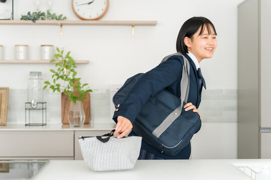 家のキッチンで通学バッグを肩にかけて笑顔で登校する制服姿の女子高校生
