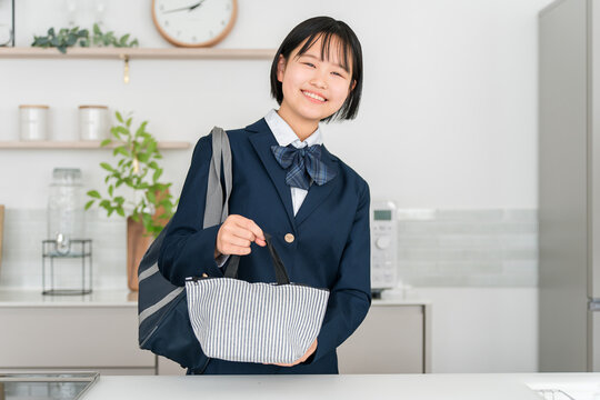 家のキッチンでお弁当の入ったランチバッグを持って笑顔を見せる制服姿の女子高校生