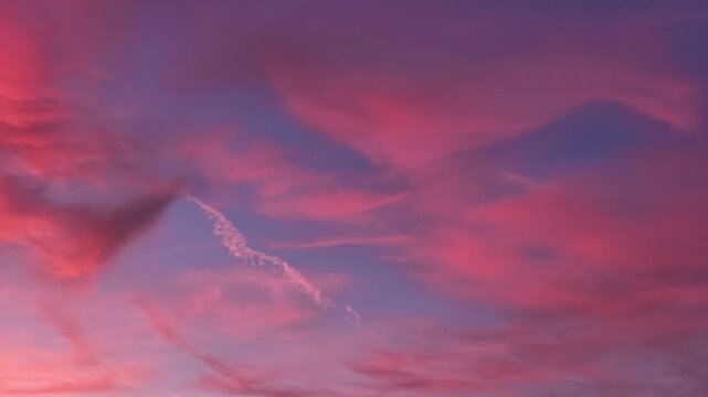 Low angle view of pink clouds and a fading contrail drifting across the sky