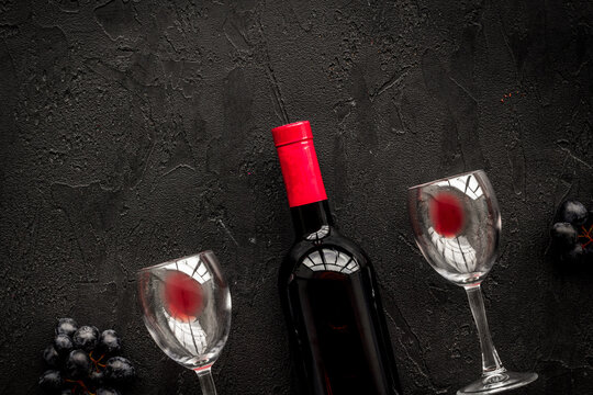 Taste red wine. Bottle of red wine, glass and black grape on black stone background top view copyspace