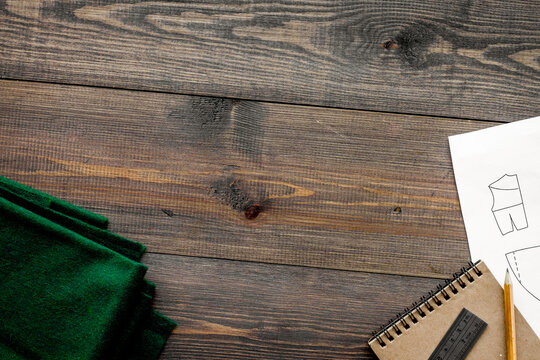 Desk of clothing designer. Textile and pattern of clothing on dark wooden background top view copyspace