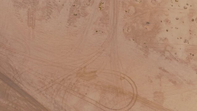 A highangle aerial view of a paved road cutting through the arid Namibian desert landscape with visible tire tracks in the sand. Great for travel, infrastructure, and environmental themes.