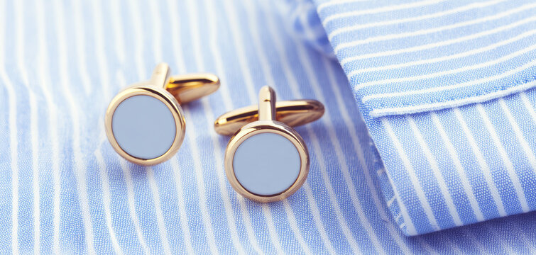 Gold cufflinks with light blue details resting on a crisp blue and white striped shirt cuff, symbolizing business attire and celebration
