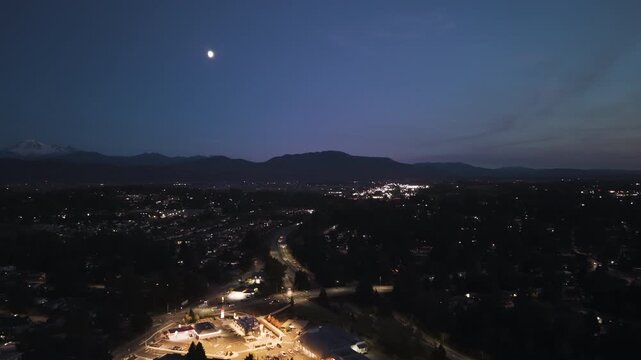 4K aerial drone view of Abbotsford, British Columbia, Canada at blue hour, showing suburban neighbourhoods, roadways and commercial areas illuminated by city lights, with mountains and Mount Baker vis