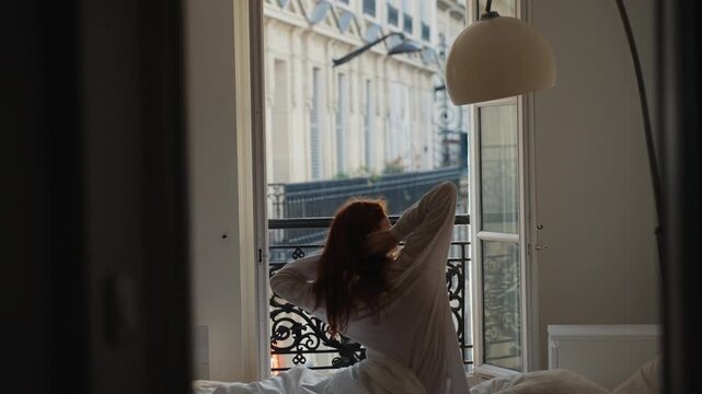 Redhead woman waking up and stretching in a parisian bedroom