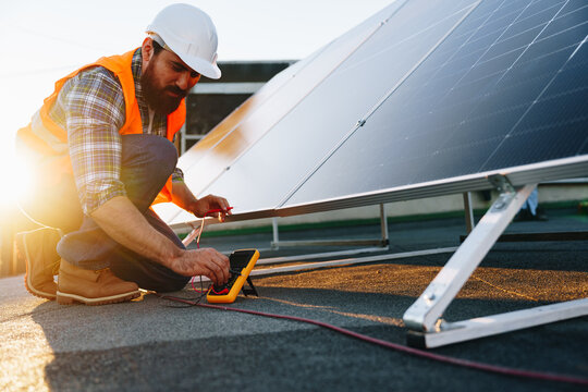 Installation of solar panels on a rooftop involves testing and monitoring equipment by a worker