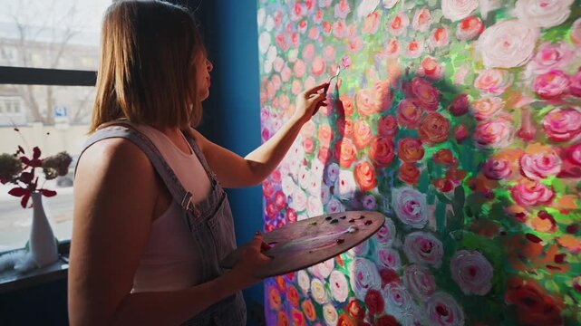 Soft sunlight falls on a painter's focused face. Her hands move with care, blending bold brushstrokes. Petals bloom in vivid pinks, oranges, and greens. She paints with passion