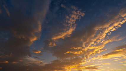 Dramatic dark clouds illuminated by golden sunlight during sunset, creating a striking contrast against the deep blue sky © banphote