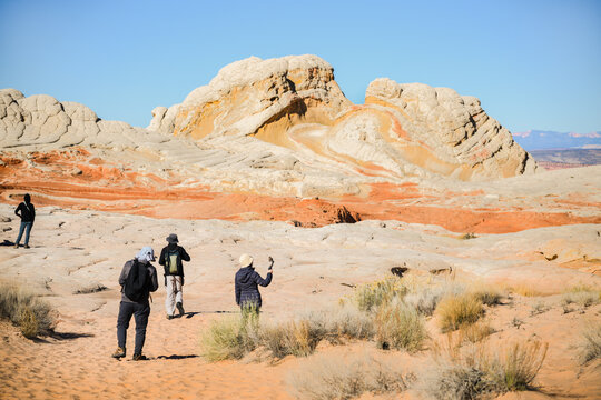 Tourists walking on the swirling and multi-coloured Navajo sandstone at White Pocket. Vermilion Cliffs National Monument. Arizona. USA.