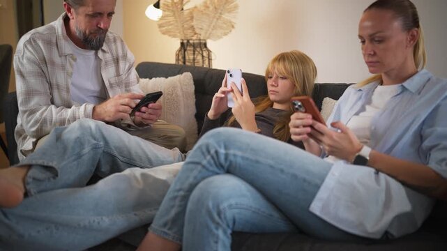 Mother, father, teenage daughter sit on sofa while use smartphones and ignoring each other. Family phone addiction, digital distraction, lack of communication, screen time,modern family relationships