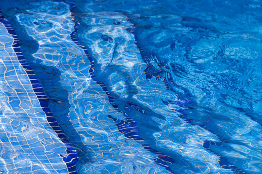 blue water surface in swimming pool with mosaic tiles and steps on floor