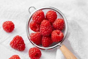 Raspberries in strainer with scattered berries for snack prep or summer dessert concept © reddish