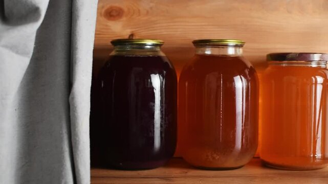 A person places a glass jar among homemade juices and compotes, then adjusts it on a wooden shelf.