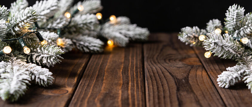 Frosted pine branches with warm fairy lights decorating a dark wooden background with large white copy space.