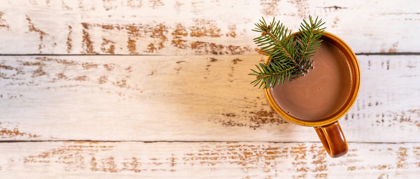 Top view of a ceramic mug with hot chocolate and a sprig of pine needles on a rustic white wooden background