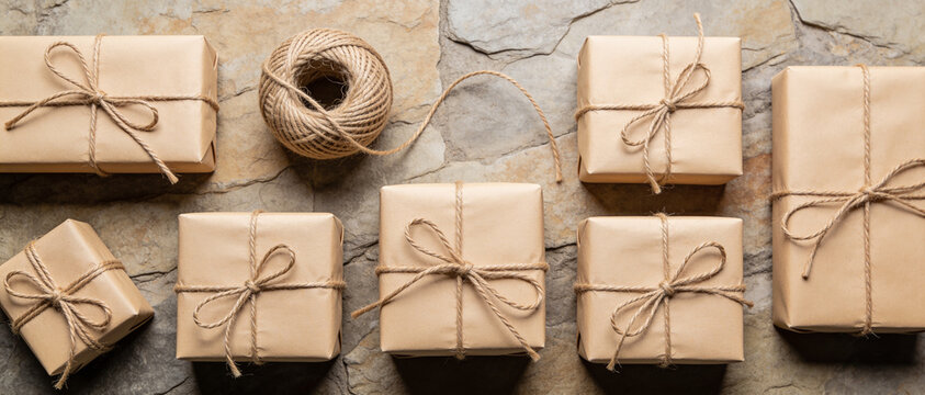 Several brown paper gift boxes tied with twine arranged on a rustic stone surface with a ball of twine from a top-down flat lay perspective